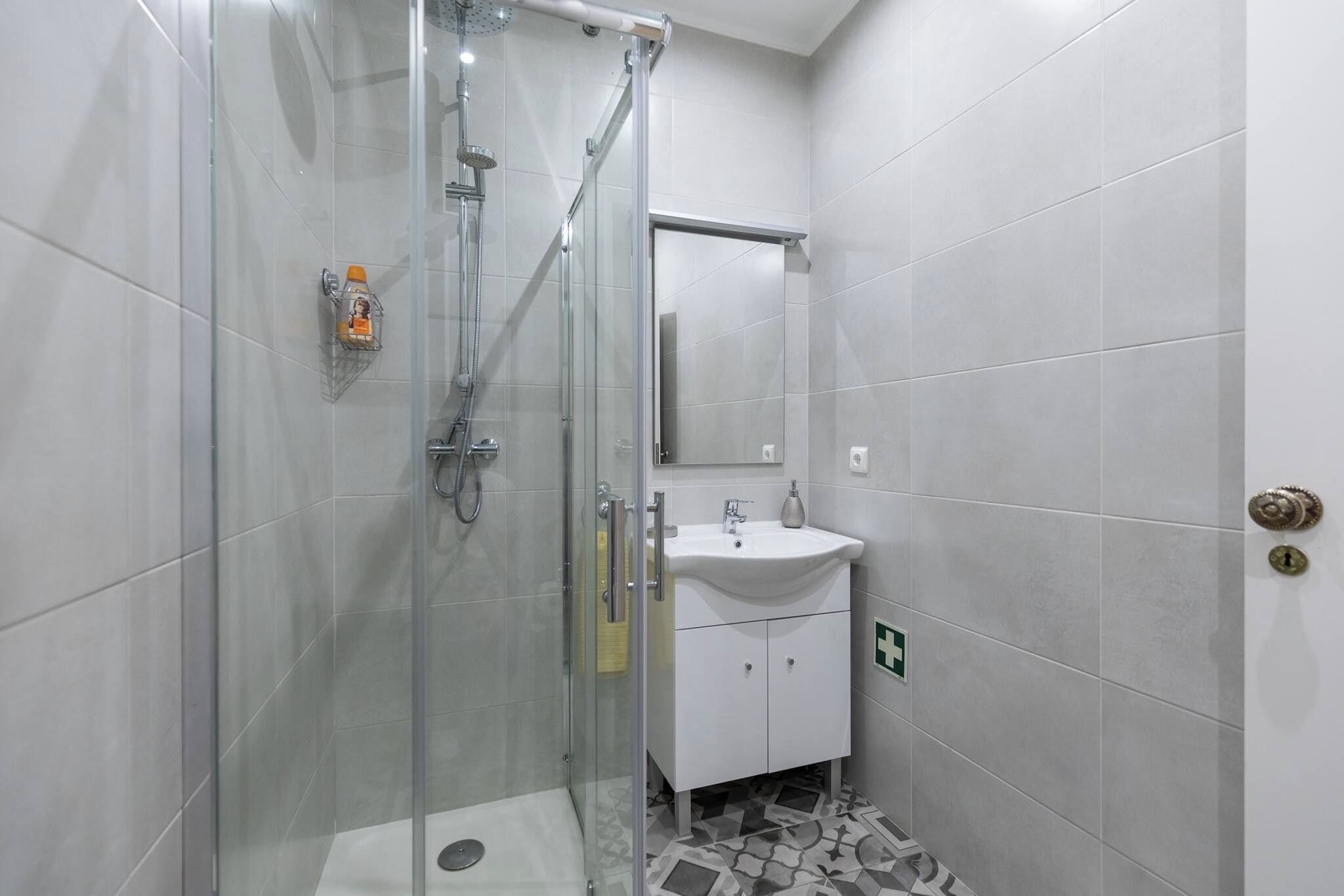 A modern bathroom with a glass-enclosed shower, a white sink, and a mirror above it.