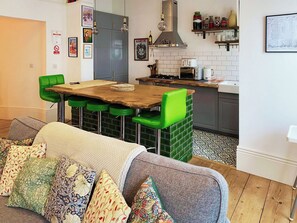 A modern kitchen with a dining area, featuring a wooden table and green bar stools. - A restored Victorian apartment blending period elegance with modern comfort. (Hastings)