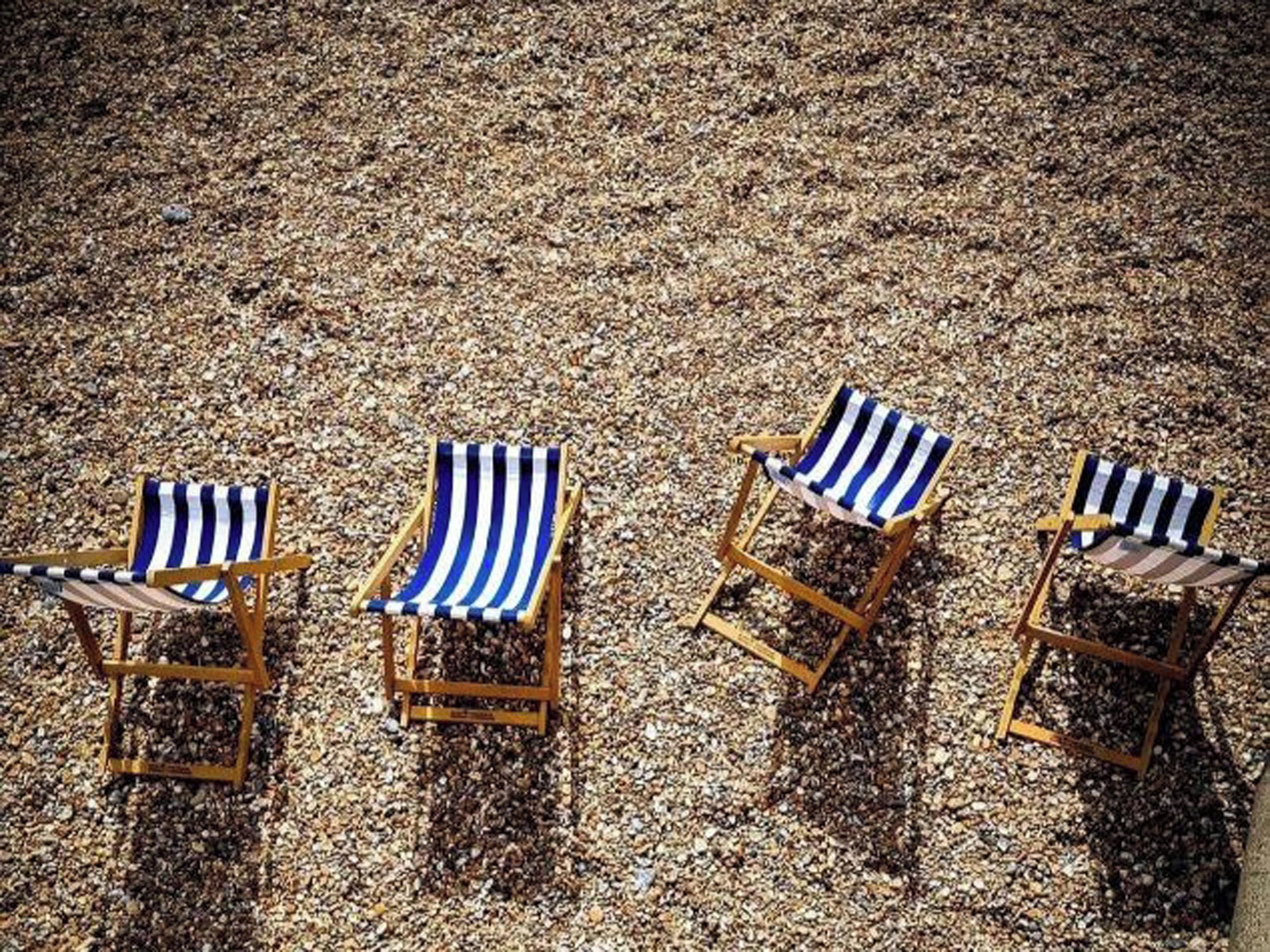 Three beach chairs with striped fabric on a pebbled surface.