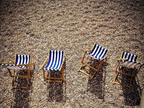 Drei Strandstühle mit gestreifter Auflage auf Kies.