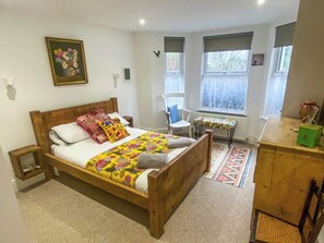 Ein Schlafzimmer mit einem hölzernen Bett, einem Sessel, einem kleinen Tisch und einem Fenster.
