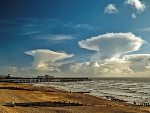 Eine Küstenlandschaft mit Strand, Wellen, einem Steg und einem bewölkten Himmel.