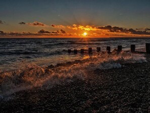 A sunset over a body of water with waves crashing onto a pebbled shore. - A restored Victorian apartment blending period elegance with modern comfort. (Hastings)