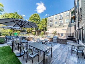 Ein möblierter Patio-Bereich im Freien mit Tischen, Stühlen, Sonnenschirmen und einem Grill.