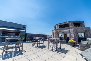 Eine Außenpatio-Terrasse mit Tischen und Stühlen, ein Backsteinbau und ein klarer, blauer Himmel.