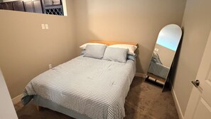 Ein Schlafzimmer mit einem Einzelbett, einem Holz-Kopfteil, einem Spiegel und einem Teppichboden.