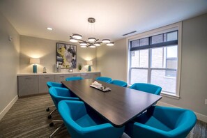 A conference room with a dark wooden table, six blue chairs, a painting on the wall, and a window with a view of buildings. - Walk to Notre Dame Stadium & Campus - Luxury 1BR, Sleeps 4 (South Bend)
