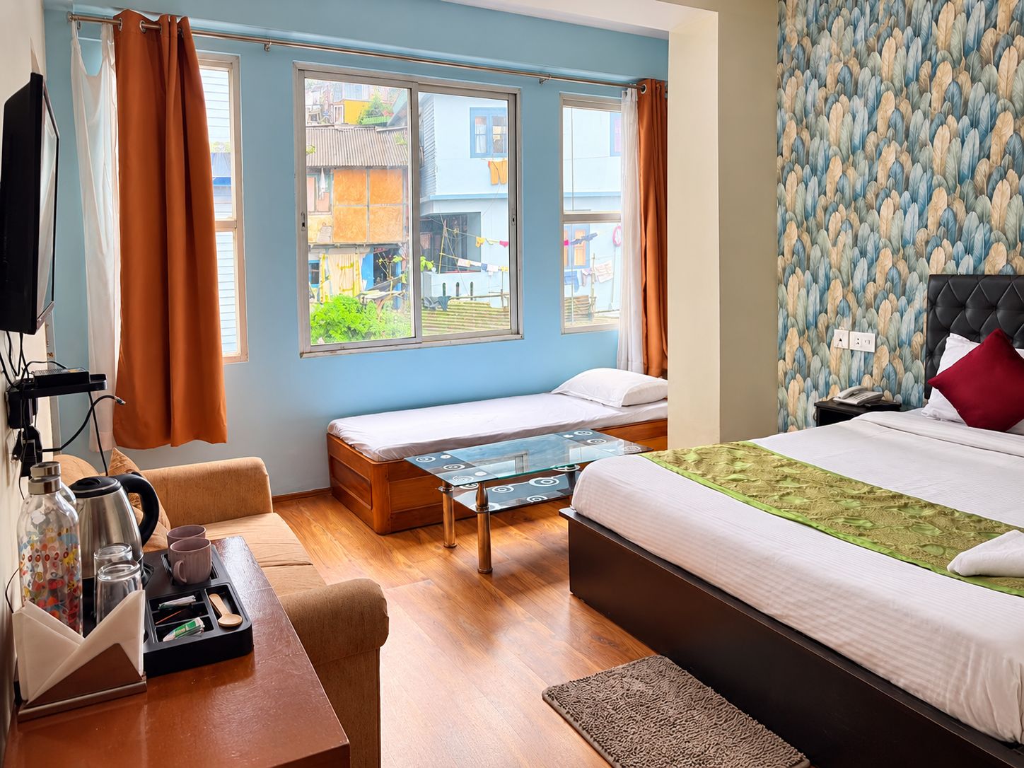 A hotel room with a bed, a sofa, a small table with a tray, a window with curtains, and a patterned wall.