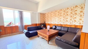A living room with a sectional sofa, a wooden coffee table, and a large window with a view of the sea. - Hotel Red Orchid  (Gangtok)