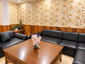 Zona d'estar moderna amb taula de cafeteria de fusta, sofàs de pell negra i un disseny de paper tapet floral.