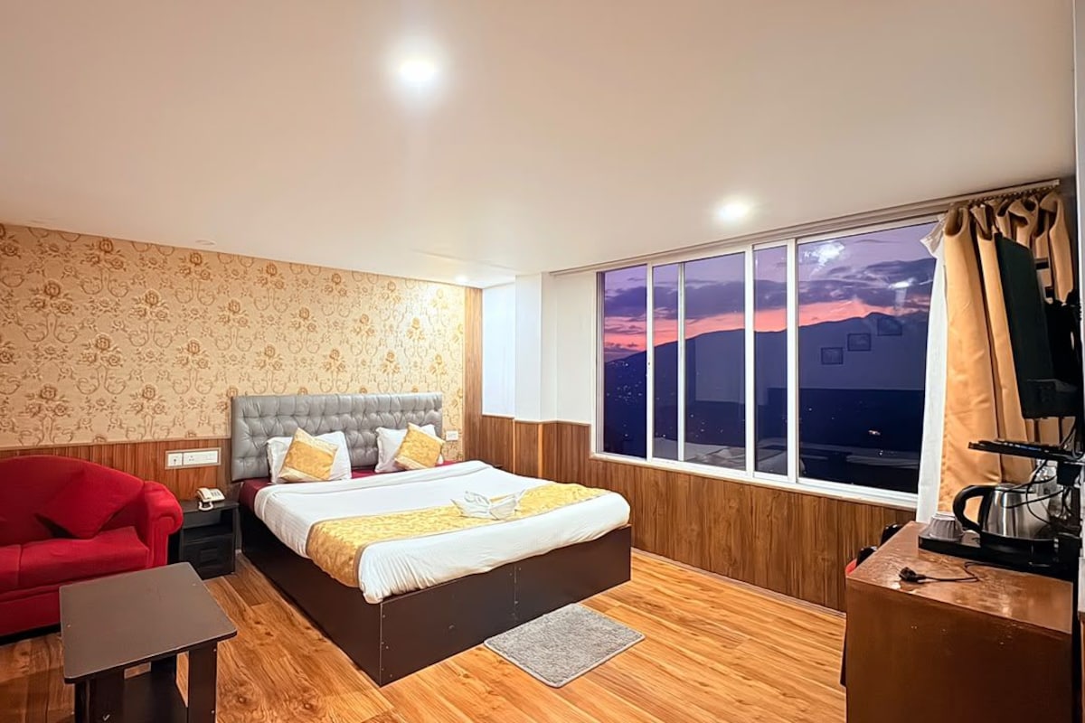 A hotel room with a bed, a red sofa, a small table, a TV, and a window with a night view.