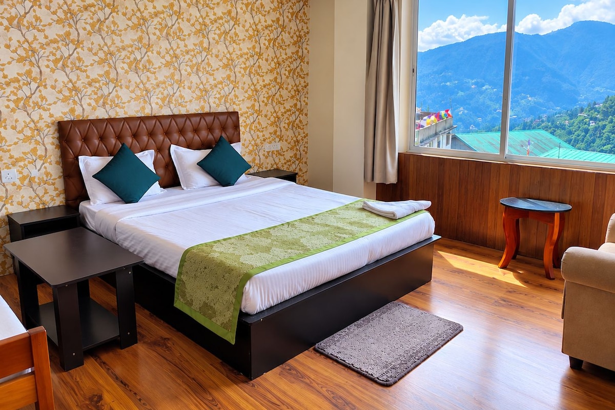 A hotel room with a large bed, a view of mountains, a wooden floor, and a small table.
