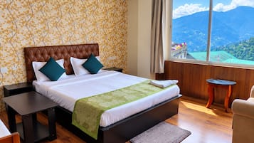 Une chambre d’hôtel avec un grand lit, une vue sur les montagnes, un plancher en bois et une petite table.