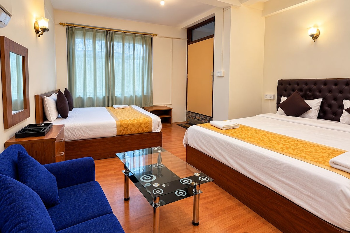 A hotel room with two beds, a sofa, a small table, and a window with curtains.