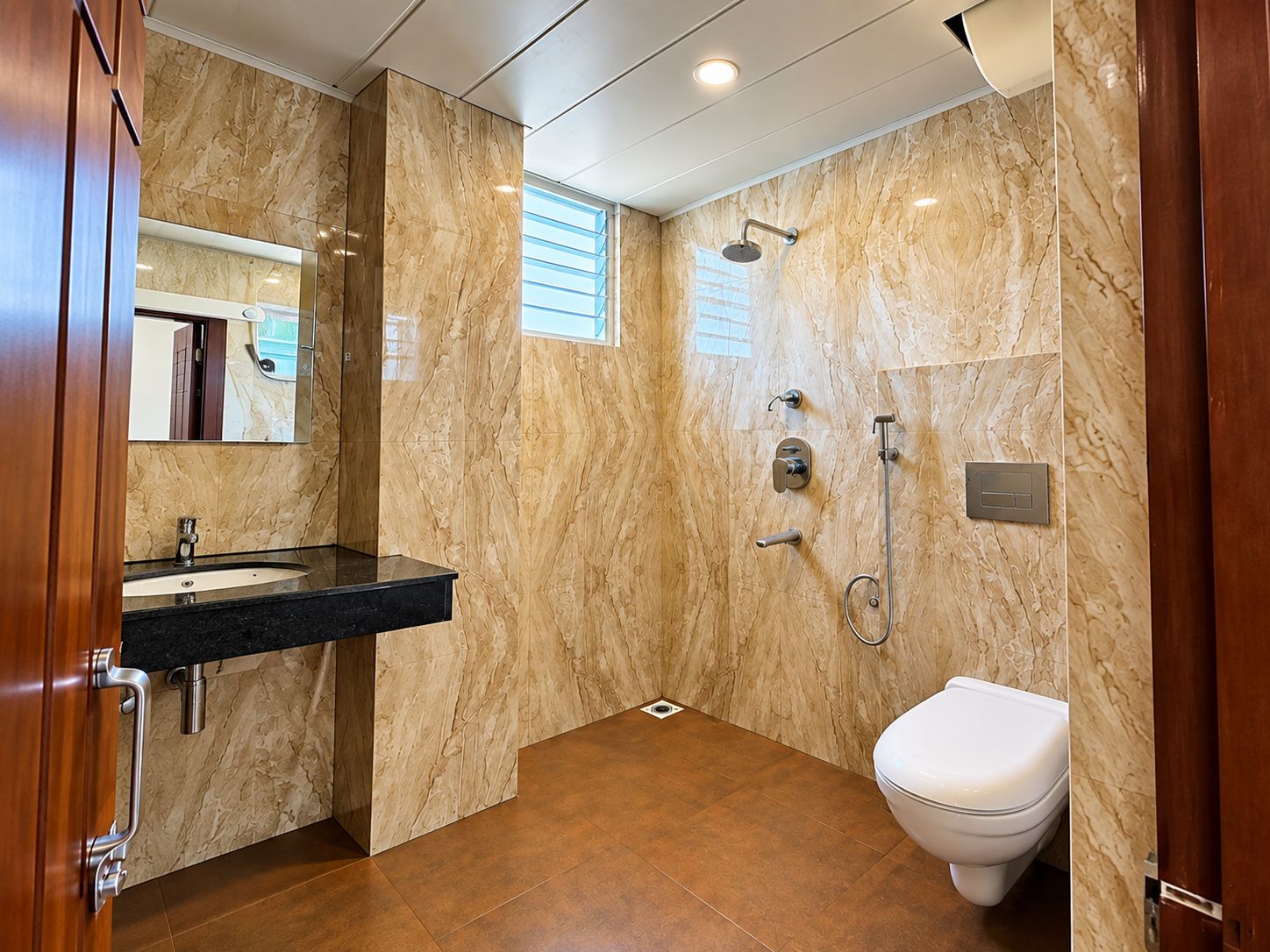 A modern bathroom with a marble wall, a black sink, a toilet, and a shower area.