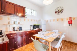 A kitchen with wooden cabinets, a microwave, a refrigerator, and a dining table with chairs. - GuestReady - Quinta A Lealdade (Arco de São Jorge)