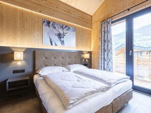 Ein Schlafzimmer mit einem großen Bett, Holzwandverkleidungen, einem Wandbild, Nachttischlampen und Blick durch eine Glastür.