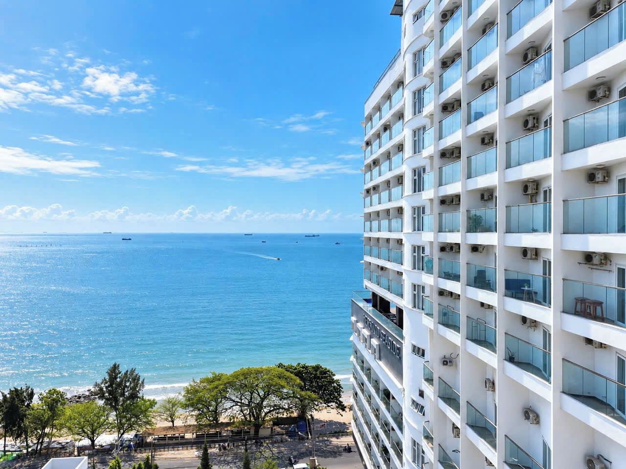 A high-rise hotel with multiple balconies overlooking a clear blue sea.