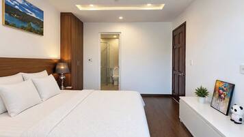 A hotel room with a bed, bedside lamp, a small plant, a framed picture, and a door leading to a bathroom.