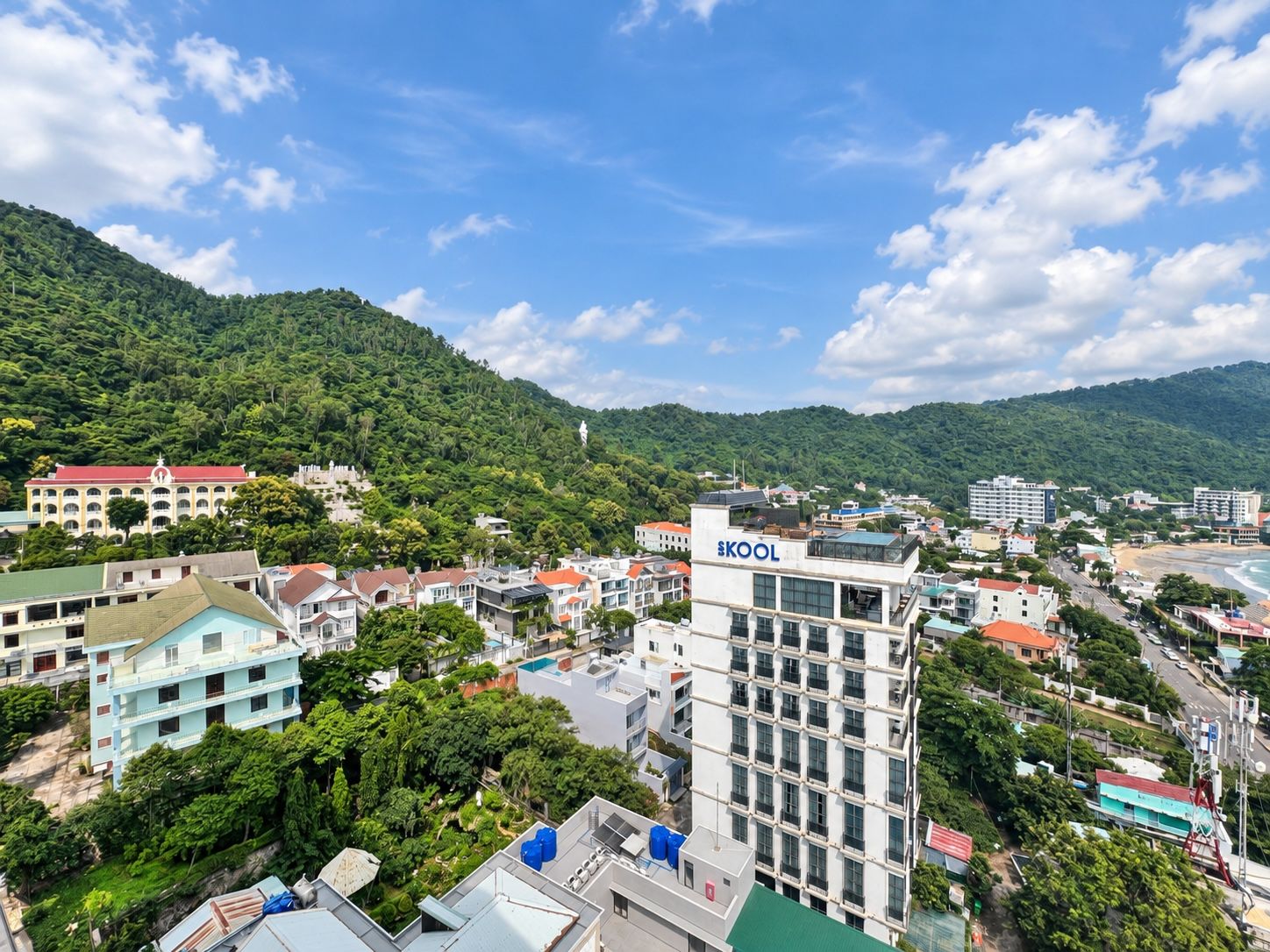 A multi-story building with a prominent 'SKOOL' sign, surrounded by residential buildings and lush greenery.