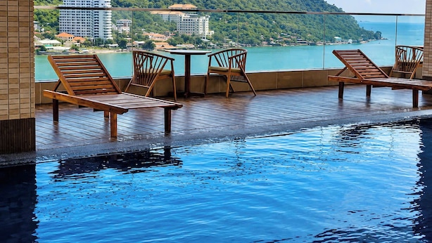 A pool area with wooden loungers and a table, overlooking a body of water and buildings. - Moc An Collection - Mermaid Seaside VT (Vung Tau)