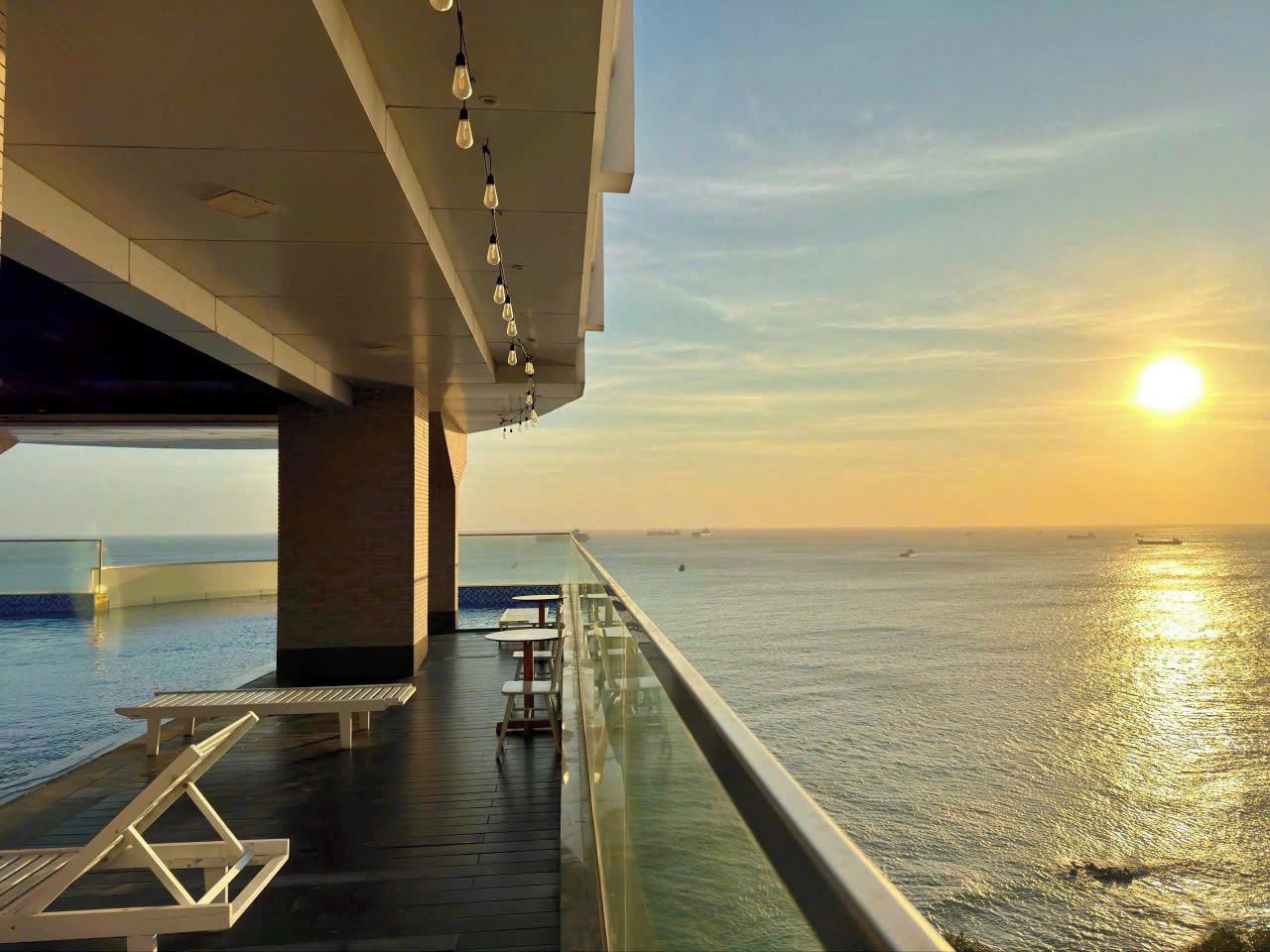 A sunlit deck with a glass barrier overlooking the sea, featuring lounge chairs and tables.