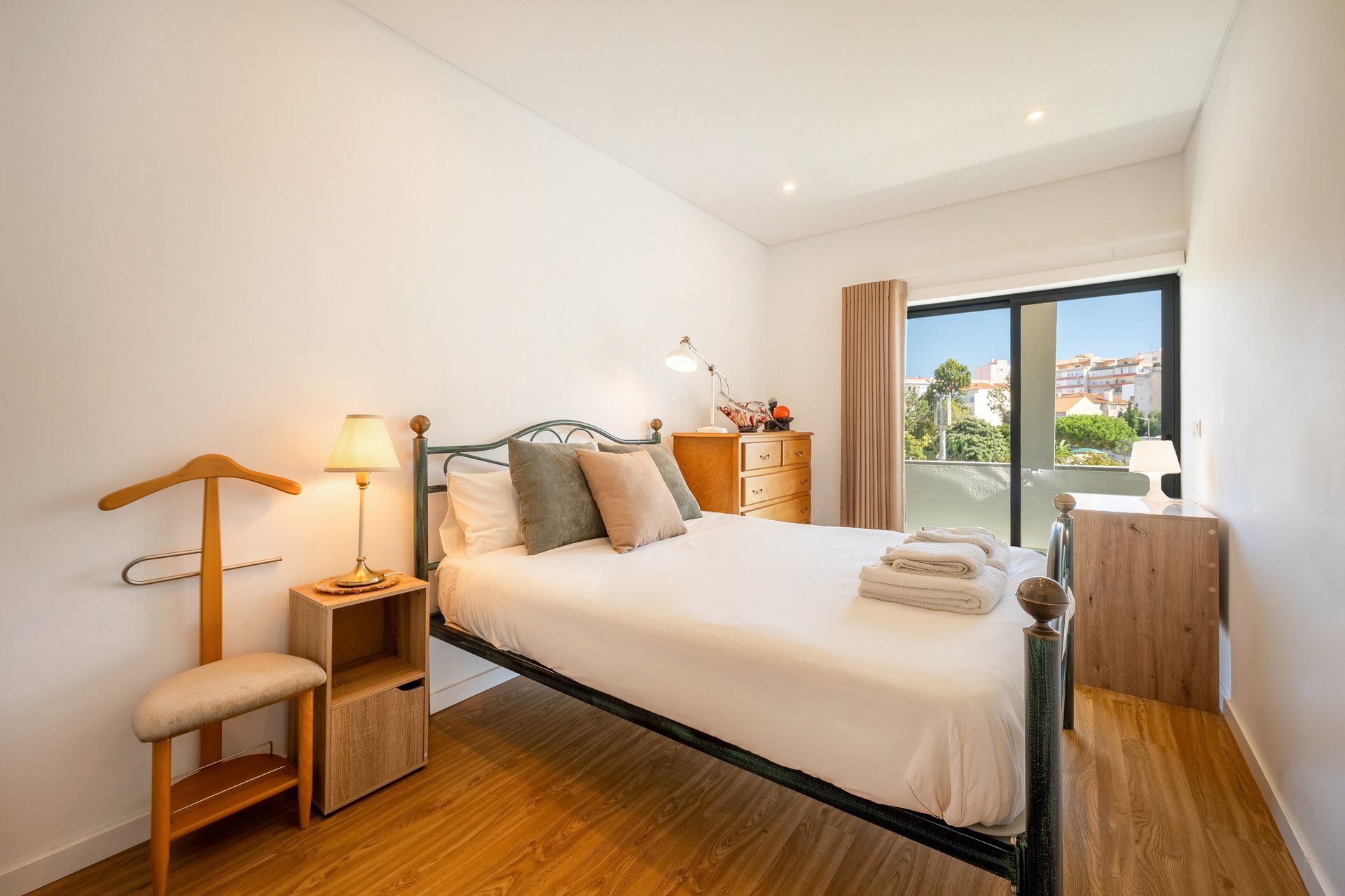 A modern bedroom with a bed, bedside table, lamp, and a view of the city through a large window.
