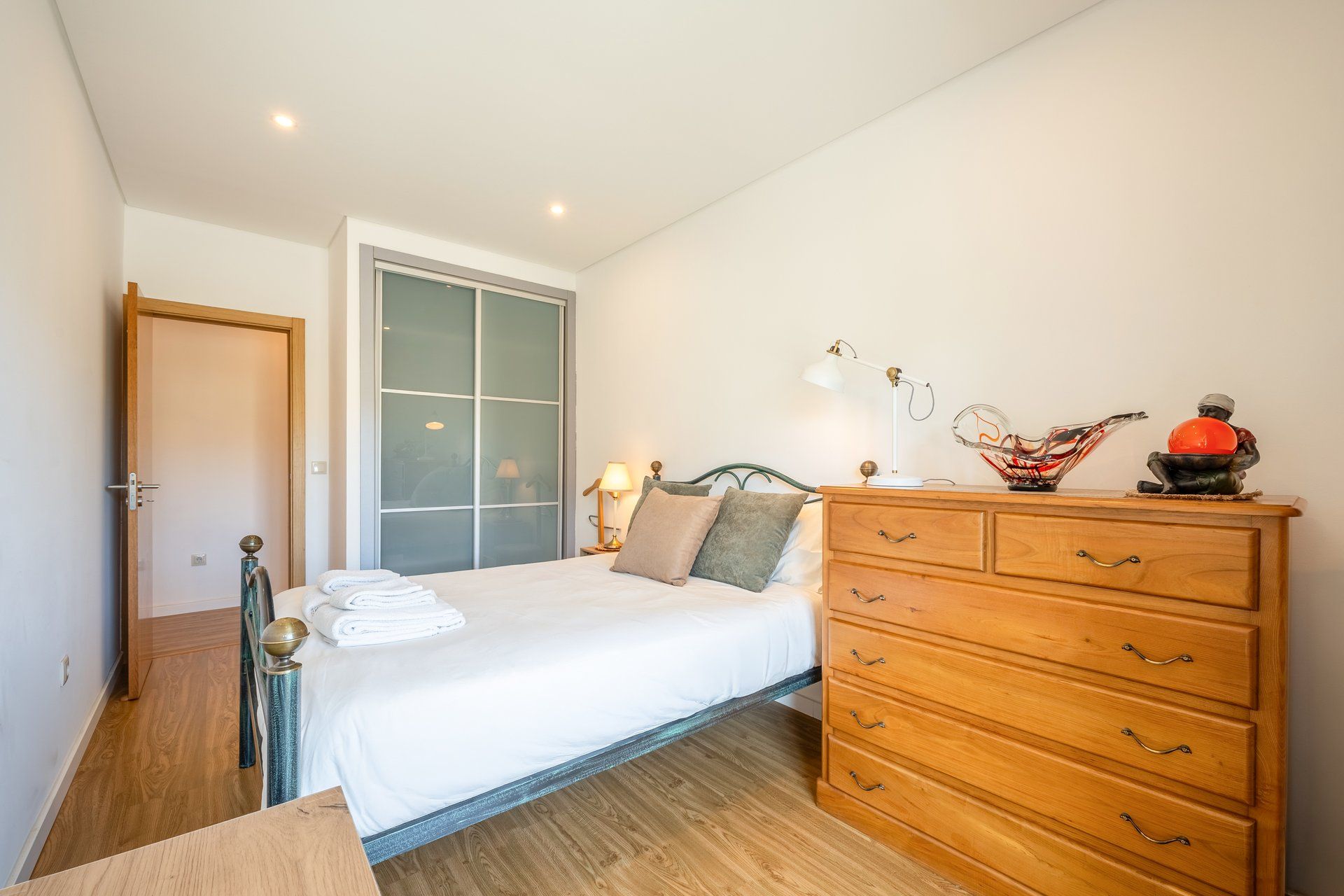 A bedroom with a bed, wooden dresser, and a large window.