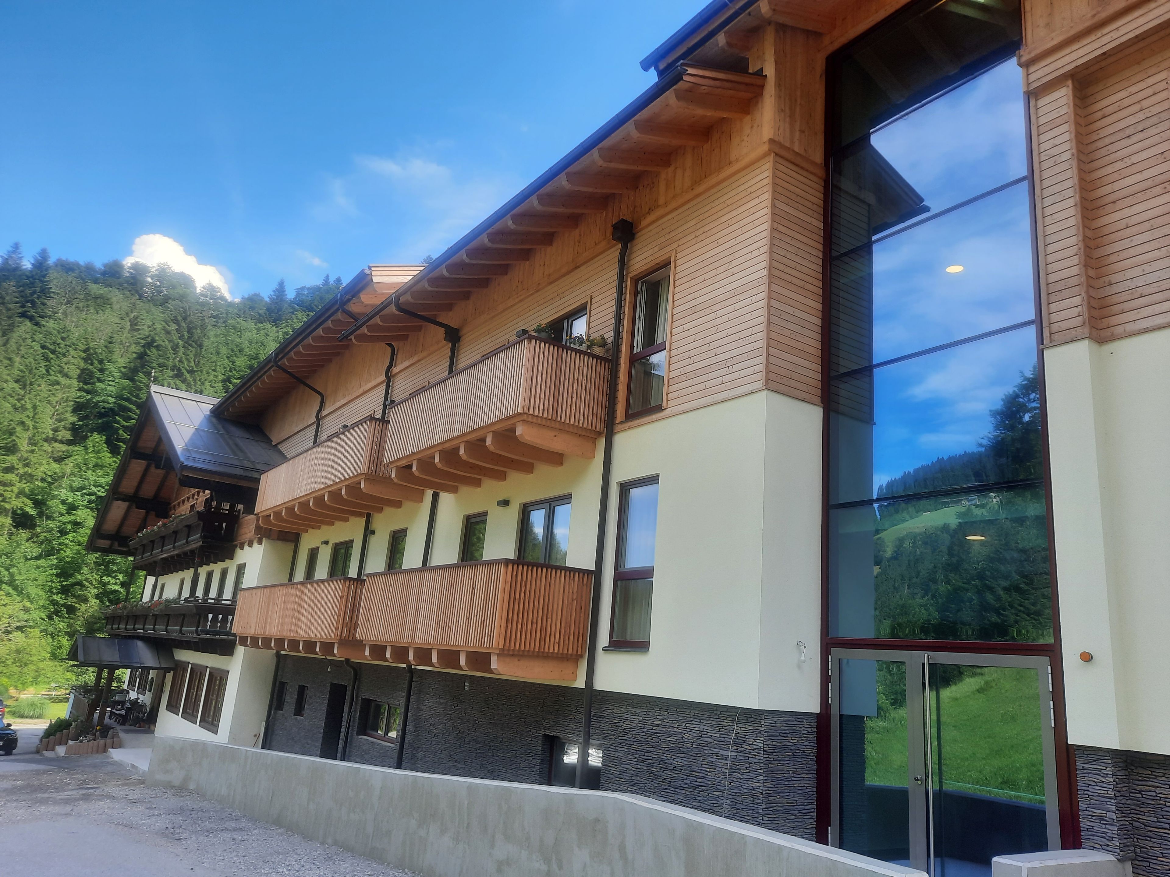 Un hotel de varios pisos con balcones de madera, ventanas grandes y vistas a una montaña boscosa.