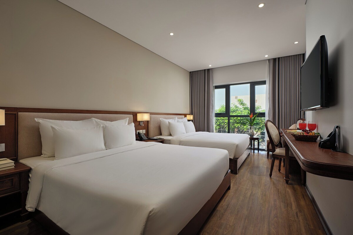 Habitación de hotel con dos camas, un escritorio, una silla, un televisor y un ventanal con vistas.