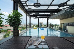 Una piscina infinita en la azotea con barandilla de cristal, una planta en maceta y una revista al borde.