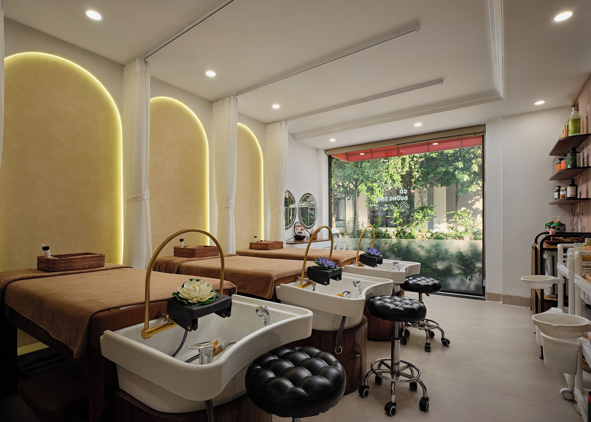 Un cuarto de spa con tres camillas de tratamiento, lavamanos individuales y vistas a la vegetación exterior.