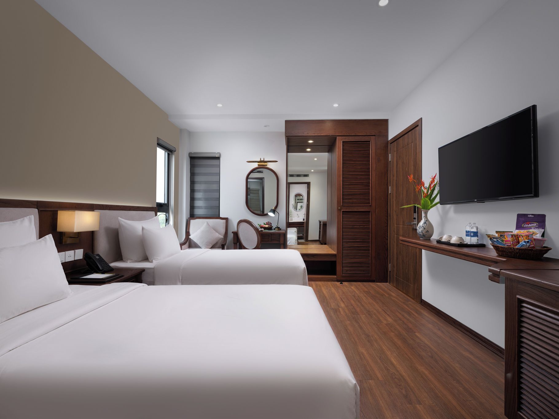 A hotel room with two beds, a desk, a mirror, a television, and a bathroom visible through an open door.