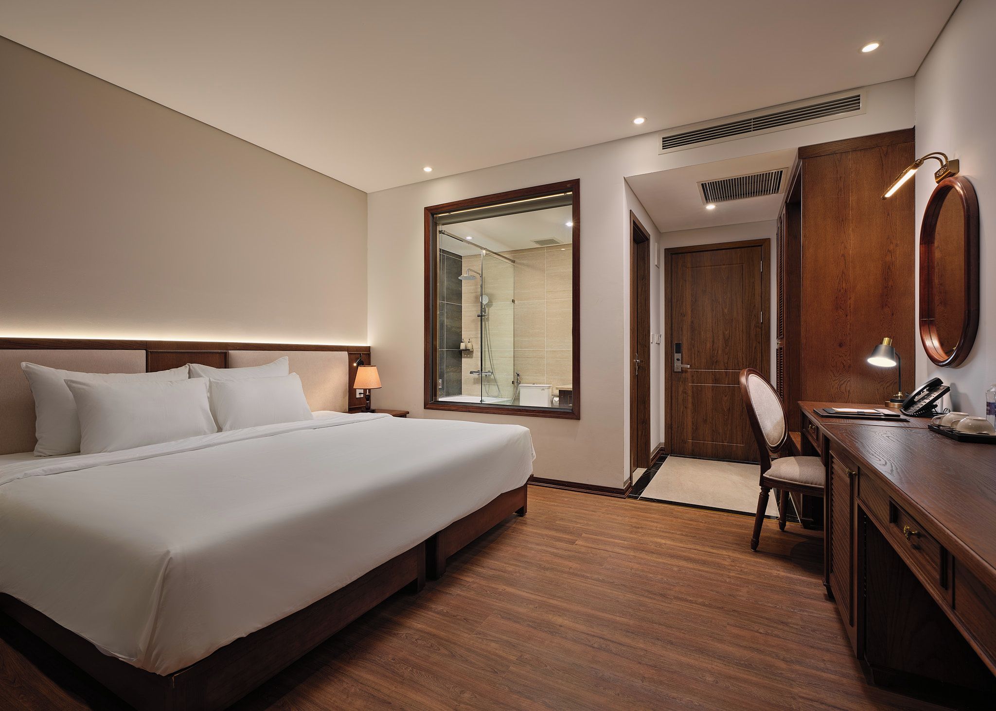 Habitación de hotel con una cama grande, un escritorio con silla, un espejo y una puerta que da a un baño.