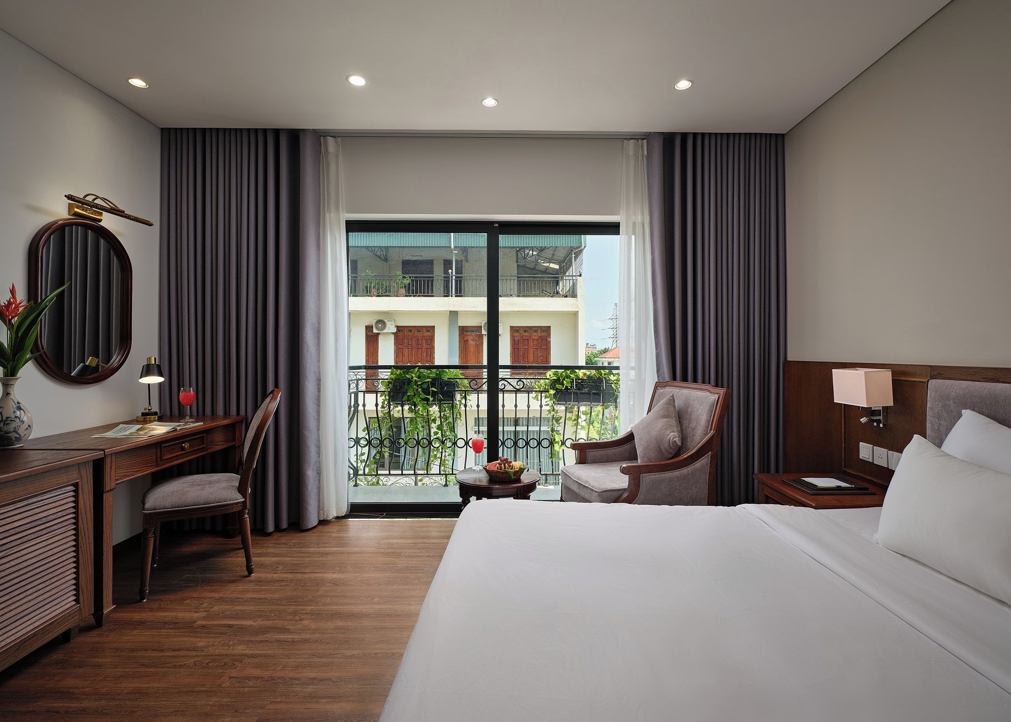 A hotel room with a bed, a desk, a chair, a nightstand, and a view of the outside.