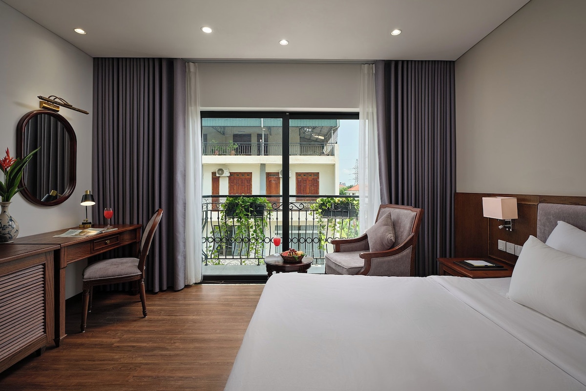 Una habitación de hotel con cama, escritorio, silla, mesita de noche y vistas al exterior.
