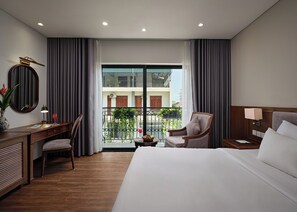 Una habitación de hotel con cama, escritorio, silla, mesita de noche y vistas al exterior.