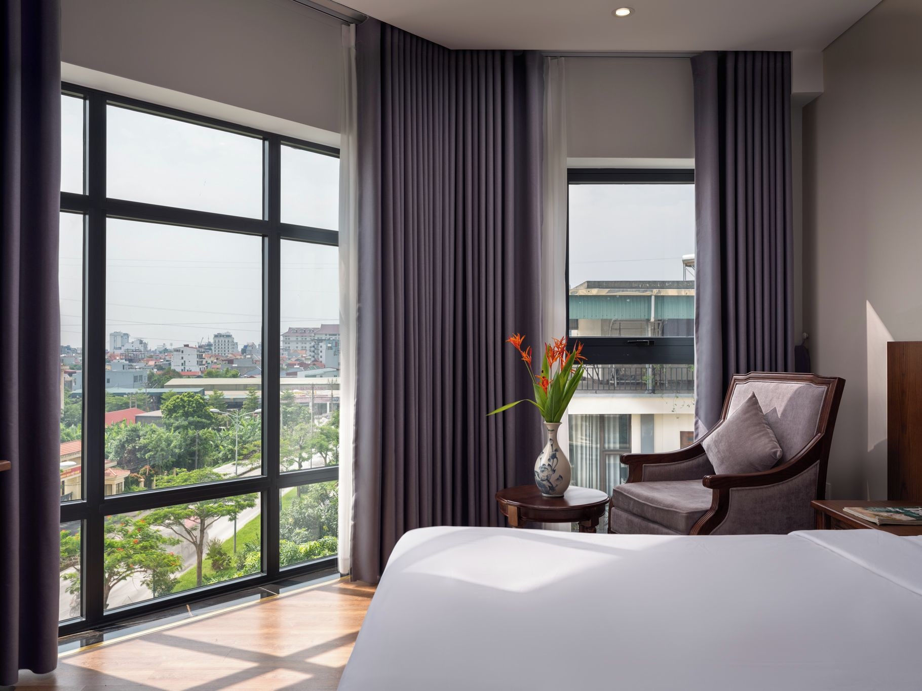 A hotel room with a large bed, a chair, a small table, and a vase with flowers.