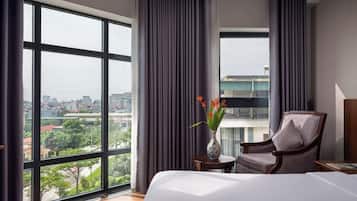 Een hotelkamer met een groot bed, een stoel, een tafeltje en een vaas met bloemen.
