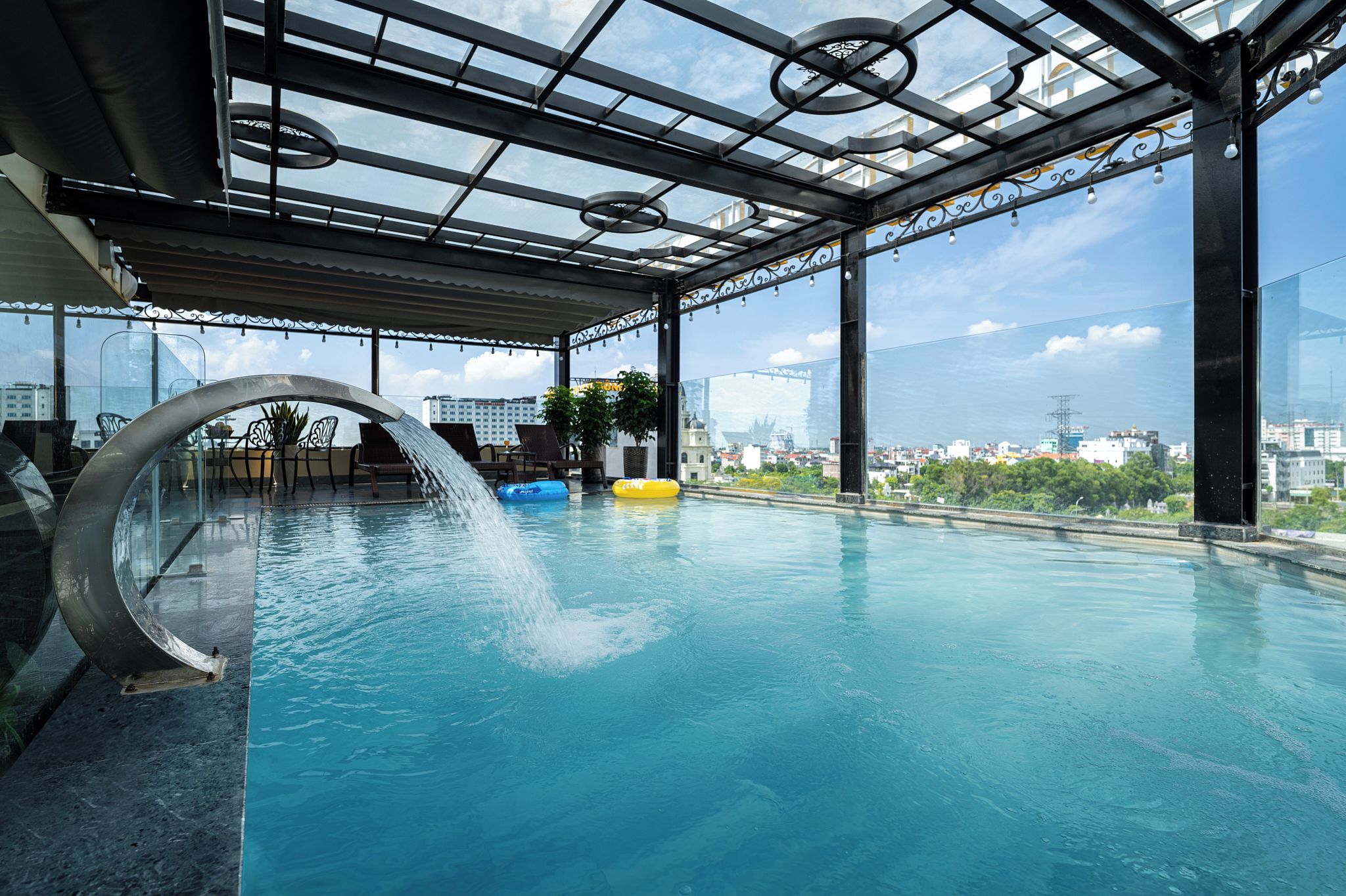 Una piscina interior con techo de cristal, agua azul cristalina y vistas a la ciudad.
