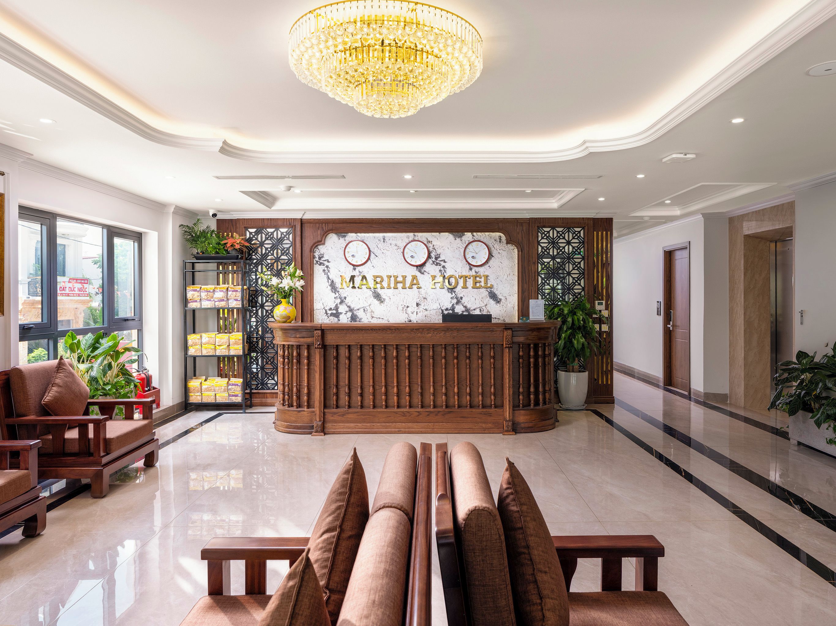 A hotel reception area with a marble floor, a wooden reception desk, a chandelier, and a large window.
