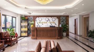 A hotel reception area with a marble floor, a wooden reception desk, a chandelier, and a large window.