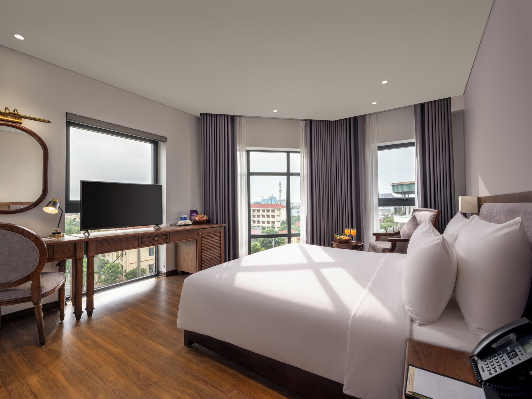 Ein Hotelzimmer mit einem großen Bett, einem Schreibtisch mit Fernseher, einem Sessel und Blick auf die Stadt.
