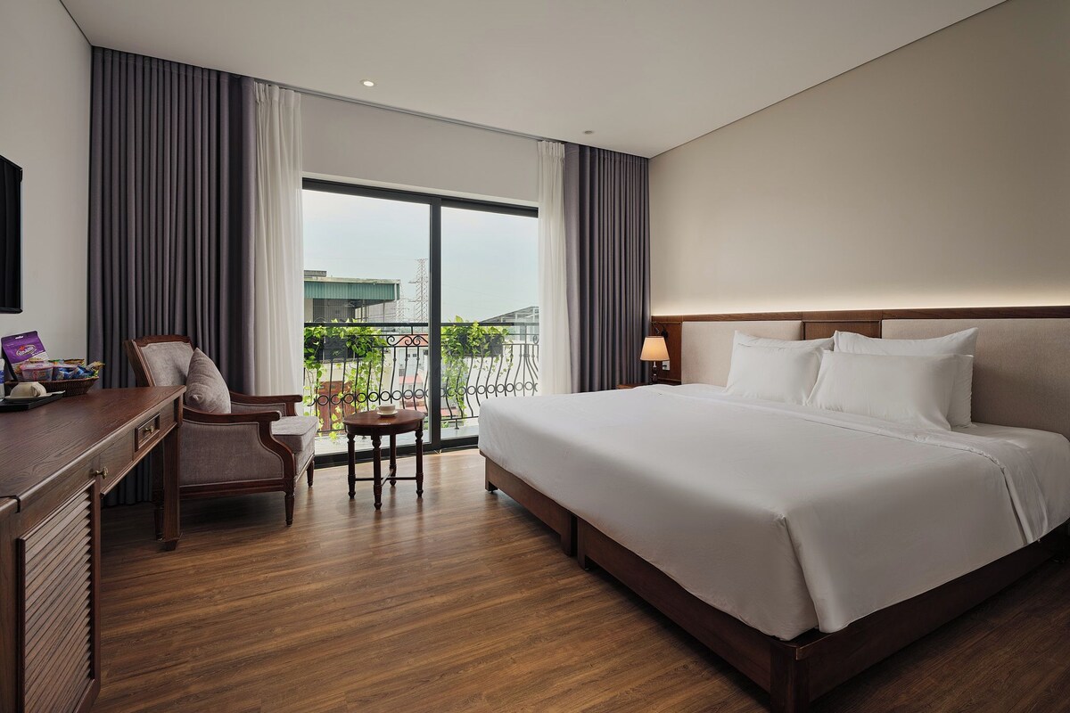 Habitación de hotel con una cama grande, un escritorio, una silla y vistas al exterior.