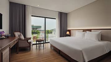 A hotel room with a large bed, a desk, a chair, and a view of the outdoors.