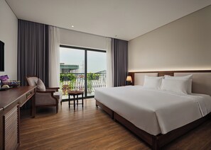 Ein Hotelzimmer mit einem großen Bett, einem Schreibtisch, einem Stuhl und Blick ins Freie.