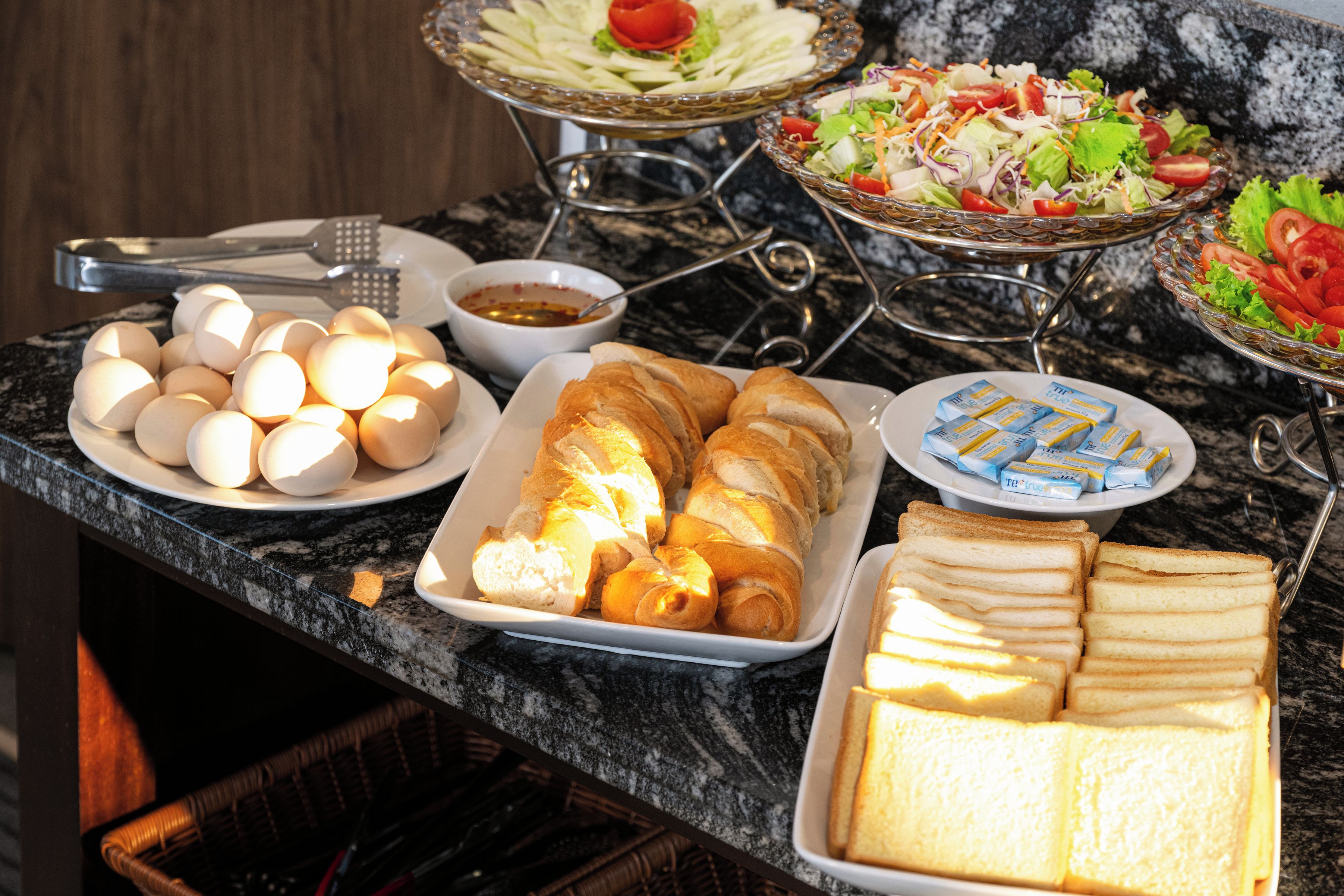 A breakfast buffet with eggs, croissants, bread, and various salads.