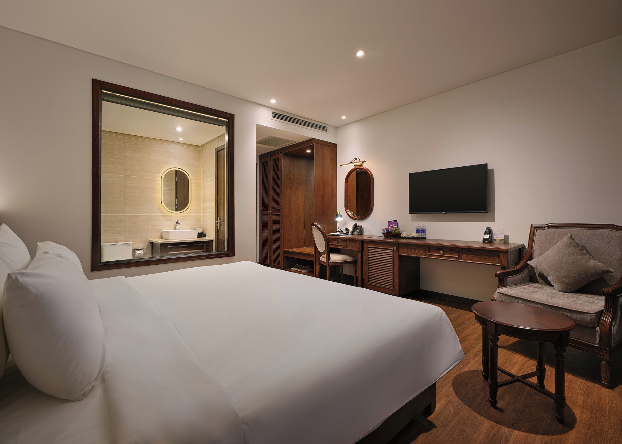 Una habitación de hotel con una cama grande, un escritorio con una silla, un televisor y un espejo.