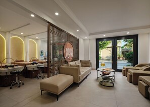 Ein moderner Wellnessraum mit einer Couch, Massagesesseln, einem Massagetisch und einem großen Fenster mit Meerblick.