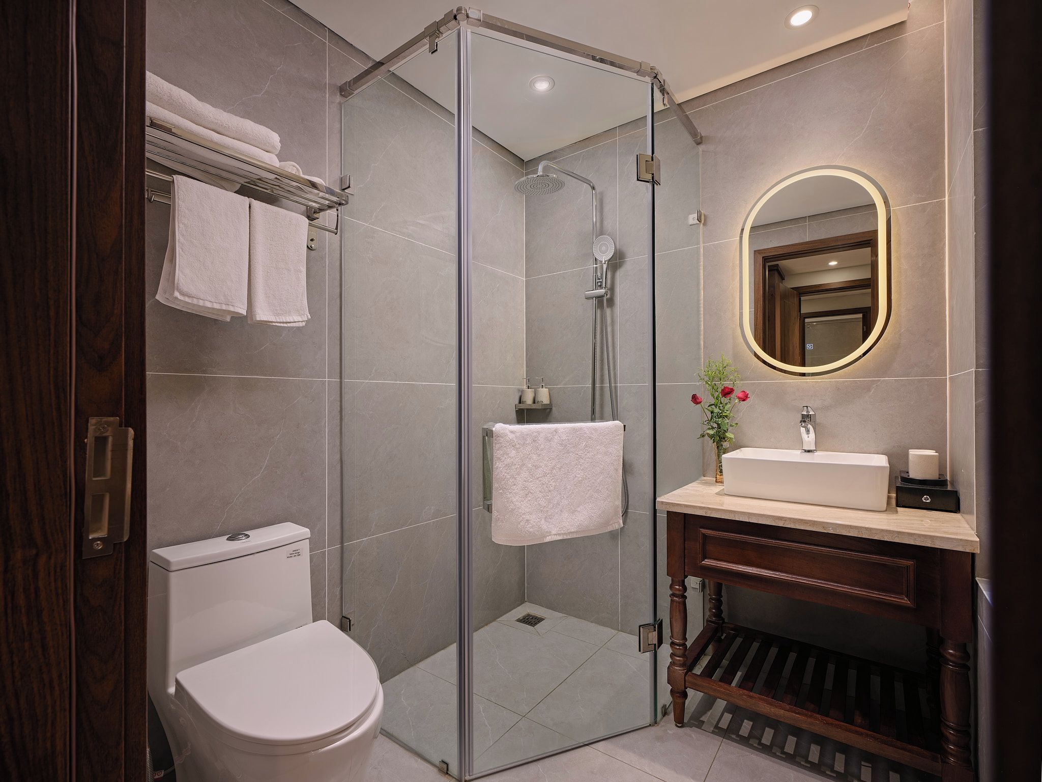 Een moderne badkamer met een douchecabine van glas, een wit toilet, een wastafel met spiegel en een wasbak.